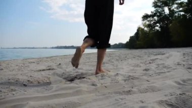 Sahilde arka planda deniz manzarasıyla koşan çıplak ayaklı bir kadın. Deniz kıyısında koşan dişi bacaklar. Mutlu bayan okyanus kıyısında vakit geçiriyor. Yaz tatili kavramı.