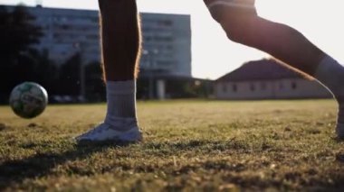 Günbatımında stadyumda futbol topu atan profesyonel futbolcuların erkek ayakları. Yeşil sahada topa vuran sporcu bacakları. Genç adamlar Meadow 'da antrenman yapıyor. Serbest stil futbol kavramı. Yavaş