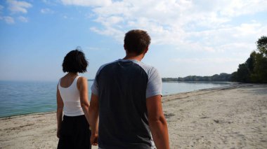 El ele tutuşup sahilde yürüyen bir çift. Güneşli bir günde deniz kıyısına giden mutlu bir çift. Sevgililer tatil köyünde birlikte vakit geçirirler. Tatil ya da tatil kavramı.