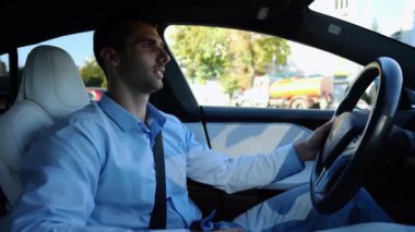 Şehir yolunda modern elektrikli araba kullanan yakışıklı bir işadamının profili. Erkek başarılı girişimci şehirde elektrikli araçla geziyor. Genç adam güneşli bir günde işe gidip geliyor. Yavaş çekim