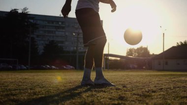 Yeşil sahada topa vuran genç adam bacakları. Günbatımında stadyumda futbol oynayan erkek futbolcu. Sporcu dışarıda numaralar yapıyor. Serbest stil futbol kavramı.