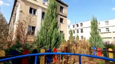 Terk edilmiş çocuk parkında atlıkarıncaya binen ve Donbass 'taki yıkık binaları gösteren bir gönüllü. Bombalı saldırılardan sonra arka planda yüksek borularda Ukrayna bayrağı sallanıyor. Yavaş