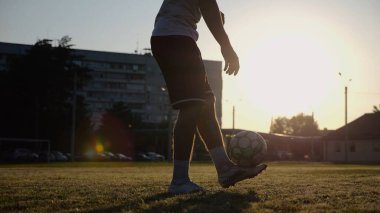 Yeşil sahada topa vuran genç adam bacakları. Günbatımında stadyumda futbol oynayan erkek futbolcu. Sporcu dışarıda numaralar yapıyor. Serbest stil futbol kavramı.