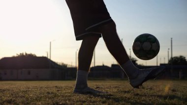 Yeşil sahada topa vuran genç adam bacakları. Günbatımında stadyumda futbol oynayan erkek futbolcu. Sporcu dışarıda numaralar yapıyor. Serbest stil futbol kavramı.
