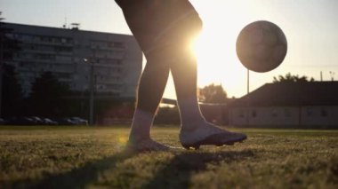 Yeşil sahada topa vuran genç adam bacakları. Günbatımında stadyumda futbol oynayan erkek futbolcu. Sporcu dışarıda numaralar yapıyor. Serbest stil futbol kavramı.