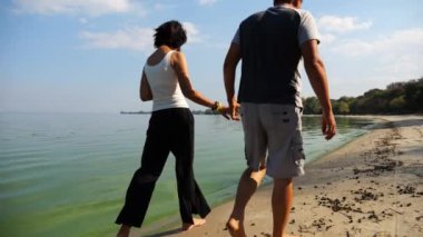 El ele tutuşup sahilde yürüyen bir çift. Güneşli bir günde deniz kıyısına giden mutlu bir çift. Sevgililer tatil köyünde birlikte vakit geçirirler. Tatil ya da tatil kavramı. Yavaş çekim