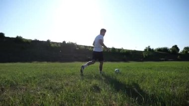 Üniformalı profesyonel futbolcu yeşil sahada koşarken topa numara yapıyor. Sporcu güneşli bir günde Meadow 'da koşarken topa vurur. Stadyumda antrenman yapan genç adam. Serbest stil futbol.