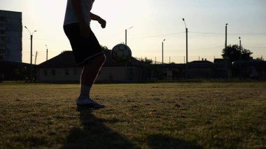 Yeşil sahada topa vuran genç adam bacakları. Günbatımında stadyumda futbol oynayan erkek futbolcu. Sporcu dışarıda numaralar yapıyor. Serbest stil futbol kavramı.