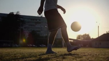 Yeşil sahada topa vuran genç adam bacakları. Günbatımında stadyumda futbol oynayan erkek futbolcu. Sporcu dışarıda numaralar yapıyor. Serbest stil futbol kavramı.