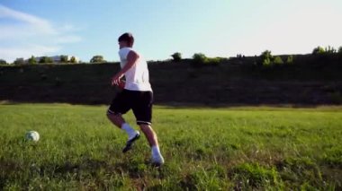 Üniformalı profesyonel futbolcu yeşil sahada koşarken topa numara yapıyor. Sporcu güneşli bir günde Meadow 'da koşarken topa vurur. Stadyumda antrenman yapan genç adam. Serbest stil futbol.