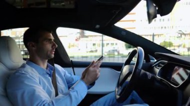 Erkek iş adamları, otomatik elektrikli araba kullanırken ciddi telefon konuşmaları yaparlar. Gergin iş adamı otomatik pilotla elektrikli otomobil kullanırken akıllı telefondan konuşur.