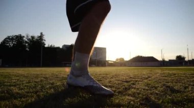 Yeşil sahada topa vuran genç adam bacakları. Günbatımında stadyumda futbol oynayan erkek futbolcu. Sporcu dışarıda numaralar yapıyor. Serbest stil futbol kavramı.