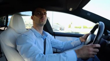 Şehir yolunda modern elektrikli araba kullanan yakışıklı bir işadamının profili. Erkek başarılı girişimci şehirde elektrikli araçla geziyor. Genç adam güneşli bir günde işe gidip geliyor. Yavaş çekim