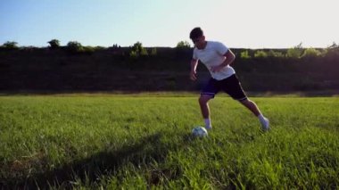 Üniformalı profesyonel futbolcu yeşil sahada koşarken topa numara yapıyor. Sporcu güneşli bir günde Meadow 'da koşarken topa vurur. Stadyumda antrenman yapan genç adam. Serbest stil futbol.