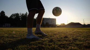 Yeşil sahada topa vuran genç adam bacakları. Günbatımında stadyumda futbol oynayan erkek futbolcu. Sporcu dışarıda numaralar yapıyor. Serbest stil futbol kavramı.