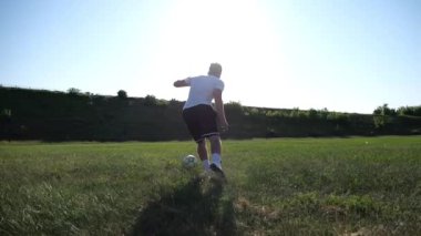 Üniformalı profesyonel futbolcu yeşil sahada koşarken topa numara yapıyor. Sporcu güneşli bir günde Meadow 'da koşarken topa vurur. Stadyumda antrenman yapan genç adam. Serbest stil futbol.