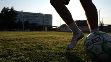 Profesyonel futbolcunun erkek ayağı, yeşil sahada koşarken topla numaralar gösterir. Sporcu bacakları gün batımında çayırda koşarken topa vurur. Stadyumda antrenman yapan genç adam. Yavaş çekim