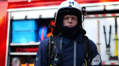 İtfaiye arabasının yanında duran kendine güveni tam bir erkek itfaiyeci portresi. Yangından sonra büyük kırmızı kamyonun arka planında baltayla poz veren tam teçhizatlı genç itfaiyeci. Kahramanlık mesleği..