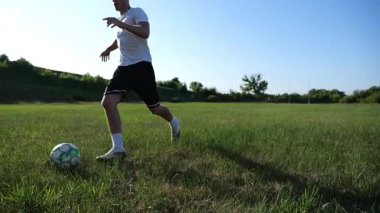 Üniformalı profesyonel futbolcu yeşil sahada koşarken topa numara yapıyor. Sporcu güneşli bir günde Meadow 'da koşarken topa vurur. Stadyumda antrenman yapan genç adam. Serbest stil futbol.