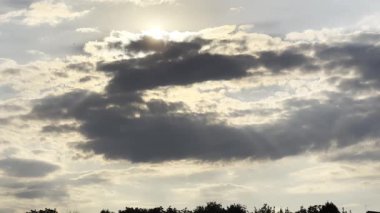 Gün batımında kümülüs bulutunu aşan güneş ışığı. Yaz günü gökyüzünde gri bulutların ardında güneş batıyor. Güzel bir doğa geçmişi var. Yavaşla.