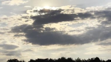 Gün batımında kümülüs bulutunu aşan güneş ışığı. Yaz günü gökyüzünde gri bulutların ardında güneş batıyor. Güzel bir doğa geçmişi var. Yavaşla.