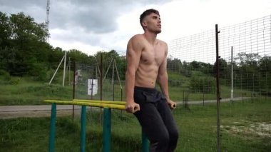 Spor alanında paralel barlarda karın kaslarını çalıştıran güçlü bir adam. Genç üstsüz sporcu doğada egzersiz yapıyor. Doğada spor yapan sporcu. Aktif spor yaşam tarzı kavramı.
