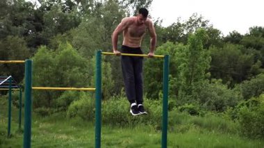 Güçlü ve kaslı bir adam doğanın yatay çubuğunda egzersiz yapıyor. Spor sahasında sıkı gömleksiz sporcu. Genç atletik adam dışarıda egzersiz yapıyor. Sağlıklı yaşam tarzı kavramı.
