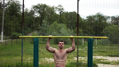 Cesur üstsüz sporcu doğadaki paralel parmaklıklar üzerinde egzersiz yapıyor. Spor alanında çalışan güçlü ve kaslı bir adam. Genç atletik adam dışarıda egzersiz yapıyor. Aktif sağlıklı yaşam tarzı kavramı.