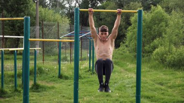 Spor sahasında karın kaslarını çalıştıran güçlü bir adam. Genç sporcu, barfiks çekme çubuğunda egzersiz yapıyor. Doğada spor yapan sporcu. Sportif yaşam tarzı kavramı.