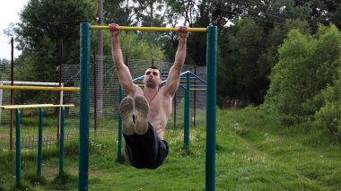 Atletik adam karın kaslarını eğitir spor sahasında yatay barda bacak kaldırır. Genç sporcu, barfiks çekme çubuğunda egzersiz yapıyor. Doğada spor yapan sporcu. Sağlıklı yaşam tarzı.