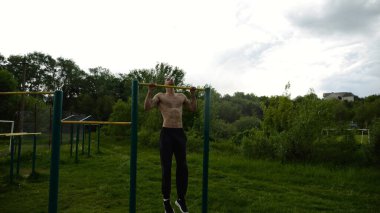 Spor sahasında barfiks çeken kaslı bir sporcu. Genç üstsüz sporcu doğada egzersiz yapıyor. Güçlü sporcu adam dışarıda antrenman yapıyor. Sağlıklı ve aktif yaşam tarzı kavramı. Yavaş