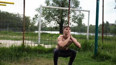 Spor sahasında çömelme hareketleri yapan erkek üstsüz atlet. Yaz doğasında çalışan genç bir sporcu. Güçlü sporcu dışarıda egzersiz yapıyor. Aktif ve sportif yaşam tarzı kavramı. Yavaş çekim