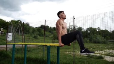 Spor alanında paralel barlarda karın kaslarını çalıştıran güçlü bir adam. Genç üstsüz sporcu doğada egzersiz yapıyor. Doğada spor yapan sporcu. Aktif spor yaşam tarzı kavramı.