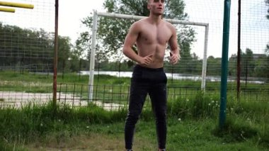 Spor sahasında çömelme hareketleri yapan erkek üstsüz atlet. Yaz doğasında çalışan genç bir sporcu. Güçlü sporcu dışarıda egzersiz yapıyor. Aktif ve sportif yaşam tarzı kavramı. Yavaş çekim