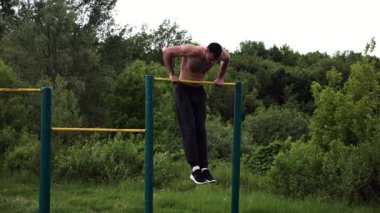 Güçlü ve kaslı bir adam doğanın yatay çubuğunda egzersiz yapıyor. Spor sahasında sıkı gömleksiz sporcu. Genç atletik adam dışarıda egzersiz yapıyor. Sağlıklı yaşam tarzı kavramı.