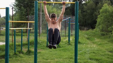 Spor sahasında karın kaslarını çalıştıran güçlü bir adam. Genç sporcu, barfiks çekme çubuğunda egzersiz yapıyor. Doğada spor yapan sporcu. Sportif yaşam tarzı kavramı.