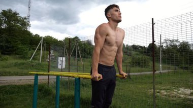 Genç sporcu doğada paralel barlarda şınav çekiyor. Spor alanında egzersiz yapan güçlü bir sporcu. Erkek üstsüz sporcu dışarıda sıkı çalışıyor. Aktif spor yaşam tarzı kavramı. Yavaş