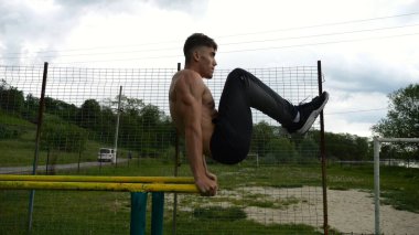 Spor alanında paralel barlarda karın kaslarını çalıştıran güçlü bir adam. Genç üstsüz sporcu doğada egzersiz yapıyor. Doğada spor yapan sporcu. Aktif spor yaşam tarzı kavramı.