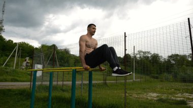 Spor alanında paralel barlarda karın kaslarını çalıştıran güçlü bir adam. Genç üstsüz sporcu doğada egzersiz yapıyor. Doğada spor yapan sporcu. Aktif spor yaşam tarzı kavramı.