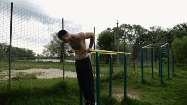 Genç sporcu doğada paralel barlarda şınav çekiyor. Spor alanında egzersiz yapan güçlü bir sporcu. Erkek üstsüz sporcu dışarıda sıkı çalışıyor. Aktif spor yaşam tarzı kavramı. Yavaş