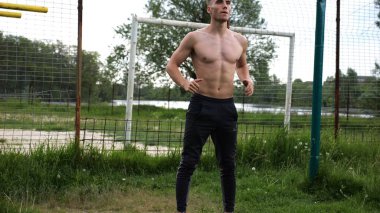 Spor sahasında çömelme hareketleri yapan erkek üstsüz atlet. Yaz doğasında çalışan genç bir sporcu. Güçlü sporcu dışarıda egzersiz yapıyor. Aktif ve sportif yaşam tarzı kavramı. Yavaş çekim