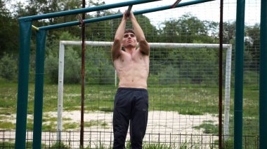 Genç kaslı sporcu spor alanında barfiks çekiyor. Atletik adam dışarıda egzersiz yapıyor. Yaz doğasında spor yapan güçlü bir adam. Sağlıklı ve aktif yaşam tarzı kavramı. Yavaş çekim