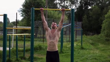 Atletik adam karın kaslarını eğitir spor sahasında yatay barda bacak kaldırır. Genç sporcu, barfiks çekme çubuğunda egzersiz yapıyor. Doğada spor yapan sporcu. Sağlıklı yaşam tarzı.