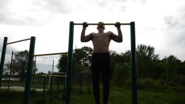 Spor sahasında barfiks çeken kaslı bir sporcu. Genç üstsüz sporcu doğada egzersiz yapıyor. Güçlü sporcu adam dışarıda antrenman yapıyor. Sağlıklı ve aktif yaşam tarzı kavramı. Yavaş