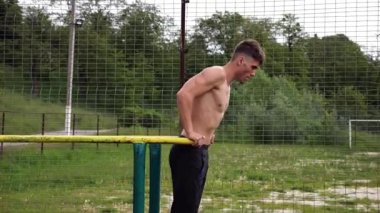 Genç sporcu doğada paralel barlarda şınav çekiyor. Spor alanında egzersiz yapan güçlü bir sporcu. Erkek üstsüz sporcu dışarıda sıkı çalışıyor. Aktif spor yaşam tarzı kavramı. Yavaş