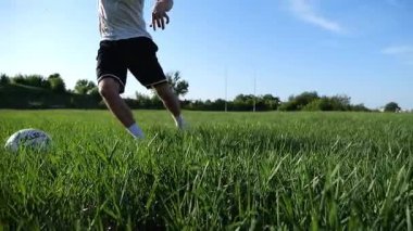 Profesyonel futbolcunun erkek ayağı, yeşil sahada koşarken topla numaralar gösterir. Güneşli bir günde Meadow 'da koşan sporcu bacakları topa vurur. Stadyumda antrenman yapan genç adam. Yavaş çekim