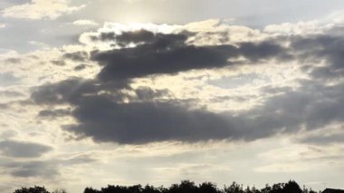 Gün batımında kümülüs bulutunu aşan güneş ışığı. Yaz günü gökyüzünde gri bulutların ardında güneş batıyor. Güzel bir doğa geçmişi var. Yavaşla.