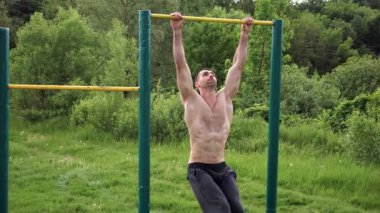 Atletik adam karın kaslarını eğitir spor sahasında yatay barda bacak kaldırır. Genç sporcu, barfiks çekme çubuğunda egzersiz yapıyor. Doğada spor yapan sporcu. Sağlıklı yaşam tarzı.