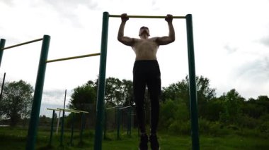 Spor sahasında barfiks çeken kaslı bir sporcu. Genç üstsüz sporcu doğada egzersiz yapıyor. Güçlü sporcu adam dışarıda antrenman yapıyor. Sağlıklı ve aktif yaşam tarzı kavramı. Yavaş