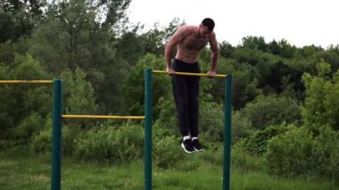 Güçlü ve kaslı bir adam doğanın yatay çubuğunda egzersiz yapıyor. Spor sahasında sıkı gömleksiz sporcu. Genç atletik adam dışarıda egzersiz yapıyor. Sağlıklı yaşam tarzı kavramı.